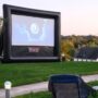 An outdoor inflatable movie screen set up on a grassy hill during sunset.